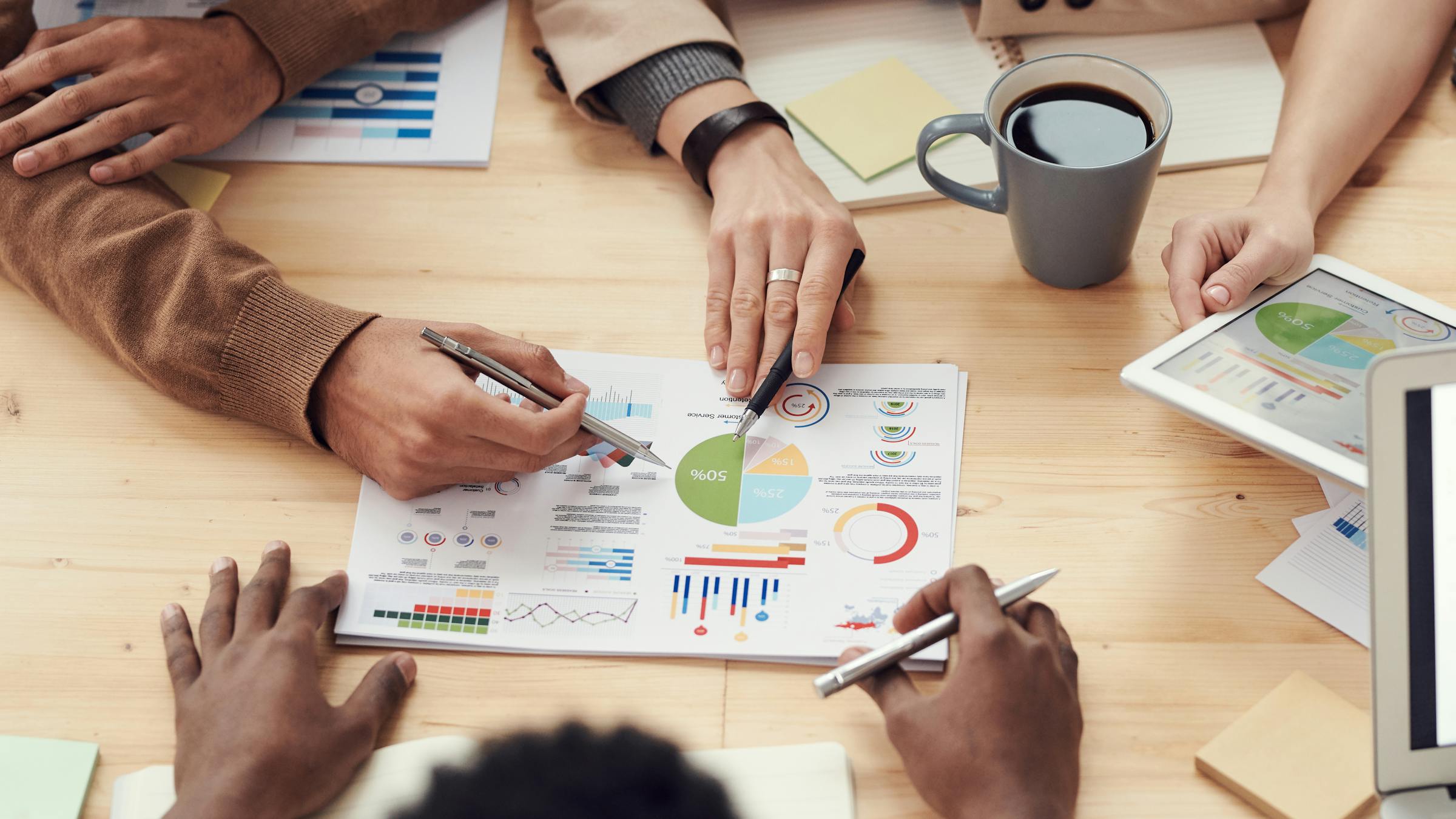 Equipo diverso colaborando alrededor de una mesa, revisando datos y compartiendo ideas en un entorno corporativo.