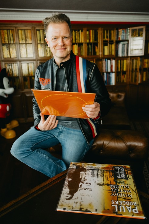 Arturo López Gavito en su estudio, sosteniendo un disco de vinilo frente a una biblioteca personal.