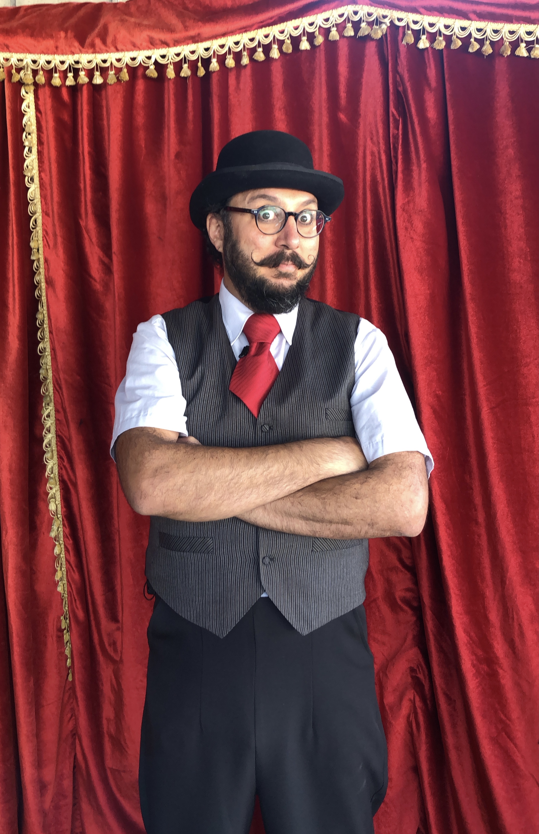 Andrés Aguilar, retrato con sombrero, chaleco y corbata roja ante telón rojo de escenario.