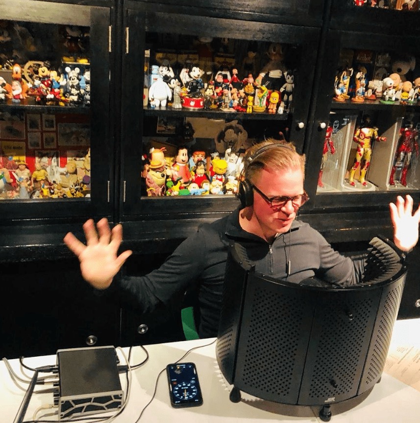 Arturo López Gavito en su estudio de grabación, gesticulando frente al micrófono con su colección al fondo.
