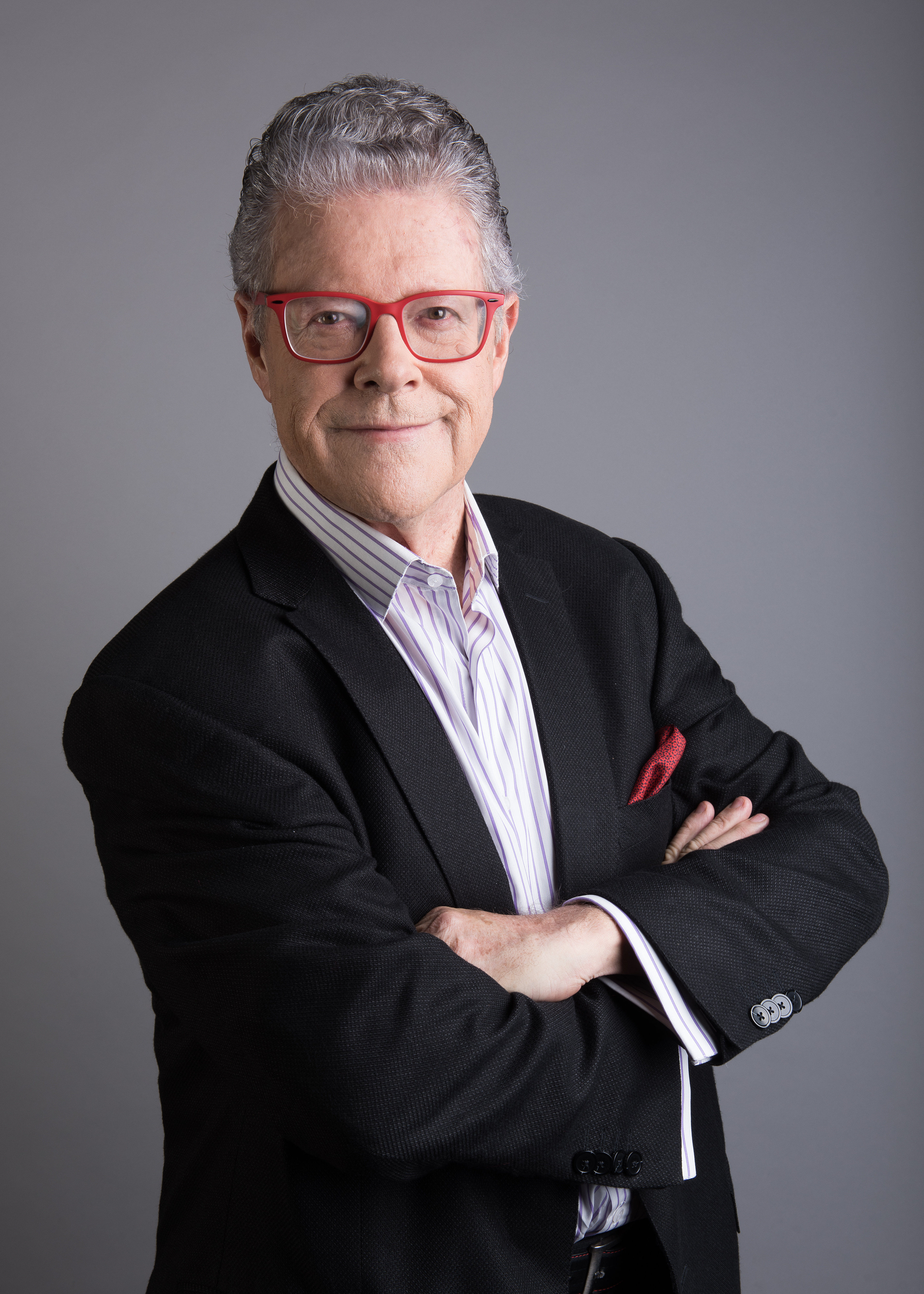 Sergio Sarmiento con traje negro y lentes rojos, brazos cruzados.